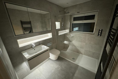 This is an example of a medium sized contemporary bathroom in Surrey with white cabinets, an alcove shower, a wall mounted toilet, grey tiles, grey walls, grey floors, an open shower, a single sink and a floating vanity unit.