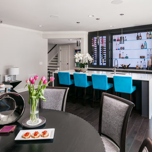 巨大なモダンスタイルのおしゃれな着席型バー (アンダーカウンターシンク、フラットパネル扉のキャビネット、黒いキャビネット、クオーツストーンカウンター、濃色無垢フローリング、茶色い床、青いキッチンカウンター、ガラス板のキッチンパネル) の写真