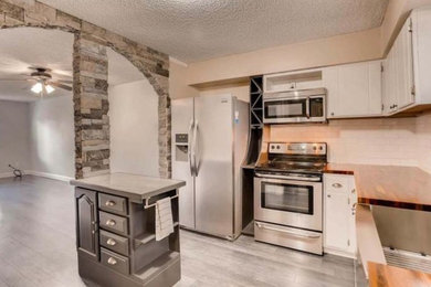Mid-sized transitional l-shaped vinyl floor and gray floor kitchen photo in Denver with a farmhouse sink, flat-panel cabinets, white cabinets, wood countertops, white backsplash, subway tile backsplash, stainless steel appliances, an island and brown countertops