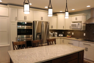 Example of a mid-sized classic u-shaped medium tone wood floor and brown floor eat-in kitchen design in Other with a farmhouse sink, shaker cabinets, white cabinets, granite countertops, brown backsplash, porcelain backsplash, stainless steel appliances and an island