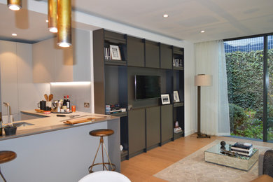 Modelo de salón abierto minimalista grande con paredes blancas, suelo de madera clara y televisor colgado en la pared