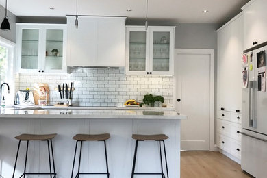 Photo of a mid-sized traditional u-shaped kitchen pantry in Melbourne with a drop-in sink, recessed-panel cabinets, white cabinets, quartz benchtops, white splashback, ceramic splashback, stainless steel appliances, light hardwood floors, with island and brown floor.