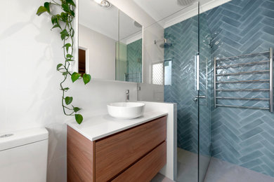This is an example of a mid-sized contemporary master bathroom in Perth with medium wood cabinets, a corner tub, a corner shower, a one-piece toilet, blue tile, ceramic tile, white walls, ceramic floors, a vessel sink, beige floor, a hinged shower door and white benchtops.