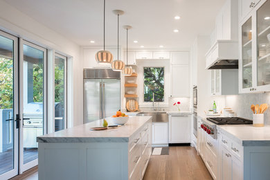 Inspiration for a transitional l-shaped medium tone wood floor and brown floor kitchen remodel in San Francisco with a farmhouse sink, shaker cabinets, white cabinets, gray backsplash, stainless steel appliances and an island
