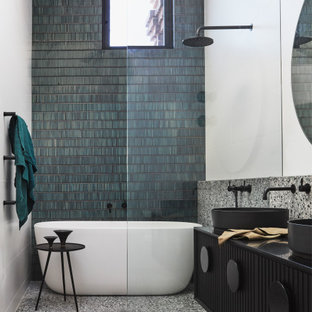 This is an example of a contemporary 3/4 bathroom in Sydney with louvered cabinets, black cabinets, a freestanding tub, an open shower, green tile, matchstick tile, white walls, ceramic floors, a pedestal sink, solid surface benchtops, multi-coloured floor, an open shower, black benchtops, a double vanity and a floating vanity.