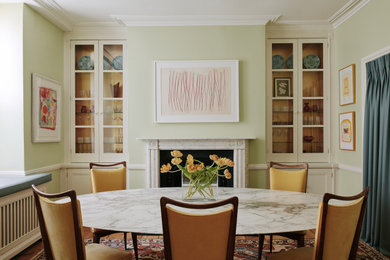 This is an example of a large eclectic enclosed dining room in London with green walls, light hardwood flooring and a stone fireplace surround.