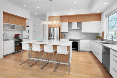 Open concept kitchen - large modern u-shaped light wood floor and brown floor open concept kitchen idea in Calgary with an undermount sink, flat-panel cabinets, white cabinets, quartz countertops, gray backsplash, matchstick tile backsplash, stainless steel appliances and an island