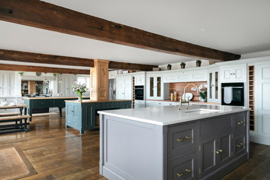 This is an example of a contemporary grey and white kitchen in Other with shaker cabinets, grey cabinets, engineered stone countertops, metallic splashback, glass sheet splashback, stainless steel appliances, dark hardwood flooring, multiple islands, brown floors, white worktops and a feature wall.