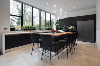 This is an example of a large contemporary l-shaped kitchen in Surrey with flat-panel cabinets, stainless steel appliances, an island, white worktops, white cabinets and concrete worktops.