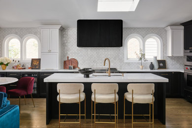 Inspiration for a transitional l-shaped medium tone wood floor and brown floor kitchen remodel in Chicago with an undermount sink, shaker cabinets, black cabinets, gray backsplash, stainless steel appliances, an island and white countertops