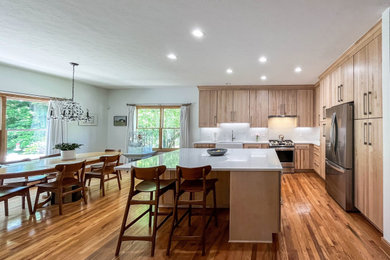 Inspiration for a mid-sized contemporary l-shaped medium tone wood floor and brown floor eat-in kitchen remodel in Cleveland with a farmhouse sink, flat-panel cabinets, light wood cabinets, quartz countertops, white backsplash, quartz backsplash, stainless steel appliances, an island and white countertops