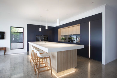 Photo of a large contemporary l-shaped open plan kitchen in Brisbane with a double-bowl sink, flat-panel cabinets, quartz benchtops, mirror splashback, black appliances, concrete floors, with island, white benchtop, black cabinets and grey floor.