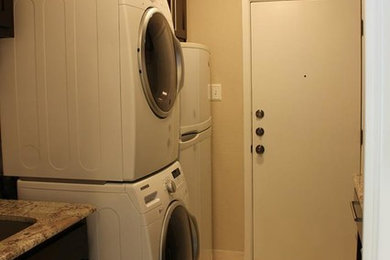 Trendy galley travertine floor laundry room photo in Dallas with an undermount sink, shaker cabinets, dark wood cabinets, granite countertops, beige walls and a stacked washer/dryer