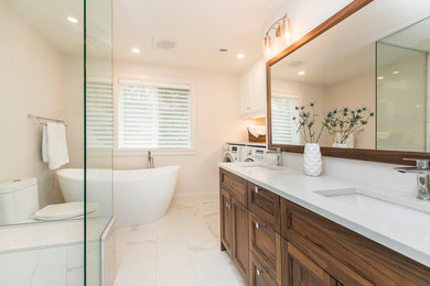 Photo of a mid-sized transitional master bathroom in Ottawa with shaker cabinets, medium wood cabinets, a freestanding tub, a one-piece toilet, white tile, porcelain tile, white walls, porcelain floors, an undermount sink, engineered quartz benchtops, white floor and white benchtops.