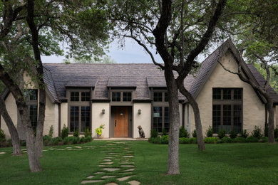 Example of a french country beige one-story stucco exterior home design in Austin with a shingle roof and a brown roof