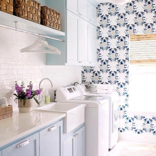 ダラスのカントリー風おしゃれなランドリールーム (エプロンフロントシンク、シェーカースタイル扉のキャビネット、青いキャビネット、淡色無垢フローリング、左右配置の洗濯機・乾燥機、ベージュの床、白いキッチンカウンター、マルチカラーの壁) の写真
