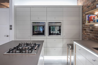 Inspiration for a mid-sized modern open plan kitchen in London with a drop-in sink, flat-panel cabinets, white cabinets, solid surface benchtops, brick splashback, stainless steel appliances, porcelain floors, with island, grey floor and grey benchtop.