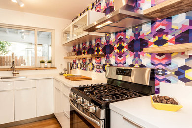 Example of a mid-sized eclectic l-shaped light wood floor eat-in kitchen design in Austin with white cabinets, multicolored backsplash, stainless steel appliances and an island