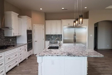 Inspiration for a mid-sized transitional l-shaped medium tone wood floor and brown floor open concept kitchen remodel in Albuquerque with a double-bowl sink, raised-panel cabinets, white cabinets, granite countertops, brown backsplash, matchstick tile backsplash, stainless steel appliances, an island and gray countertops