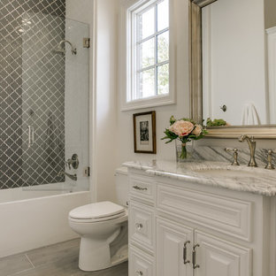 Idée de décoration pour une petite salle de bain tradition pour enfant avec un placard avec porte à panneau surélevé, des portes de placard blanches, un combiné douche/baignoire, un WC séparé, un carrelage gris, des plaques de verre, un mur blanc, un sol en carrelage de porcelaine, un lavabo encastré et un plan de toilette en marbre.