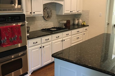 Traditional kitchen in Dallas with raised-panel cabinets, white cabinets, grey splashback, subway tile splashback, stainless steel appliances, dark hardwood floors, with island, brown floor and black benchtop.