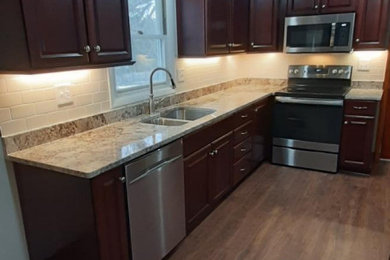 Inspiration for a timeless l-shaped laminate floor and brown floor eat-in kitchen remodel in New York with a double-bowl sink, raised-panel cabinets, dark wood cabinets, granite countertops, brown backsplash, ceramic backsplash, stainless steel appliances, no island and brown countertops