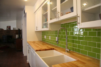 Kitchen - mid-sized farmhouse single-wall dark wood floor kitchen idea in Phoenix with a farmhouse sink, glass-front cabinets, white cabinets, wood countertops, green backsplash, subway tile backsplash, white appliances and an island