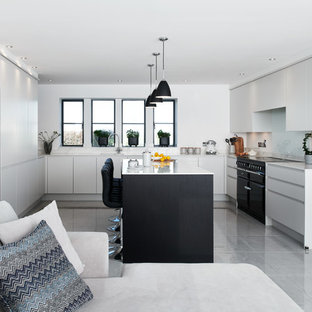 This is an example of a modern u-shaped kitchen in Wiltshire with a single-bowl sink, flat-panel cabinets, composite countertops, white splashback, glass sheet splashback, black appliances, porcelain flooring, an island, grey floors, white worktops and white cabinets.