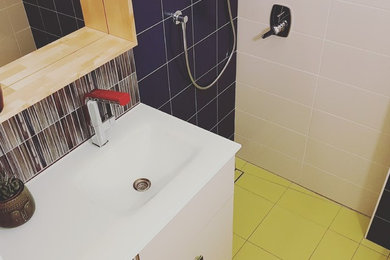 Photo of a small transitional 3/4 bathroom in Other with flat-panel cabinets, beige cabinets, a corner shower, a wall-mount toilet, multi-coloured tile, porcelain tile, multi-coloured walls, porcelain floors, a vessel sink, glass benchtops, yellow floor and a hinged shower door.
