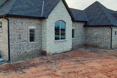 Inspiration for a large timeless beige one-story brick house exterior remodel in Oklahoma City with a hip roof and a shingle roof