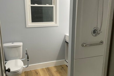 Example of a small farmhouse master vinyl floor, brown floor and single-sink bathroom design in Other with white cabinets, a one-piece toilet, gray walls, a drop-in sink, white countertops, a freestanding vanity and shaker cabinets
