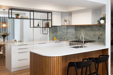 This is an example of a medium sized contemporary u-shaped kitchen/diner in Brisbane with a submerged sink, flat-panel cabinets, white cabinets, engineered stone countertops, green splashback, porcelain splashback, integrated appliances, light hardwood flooring, a breakfast bar, brown floors, white worktops and a coffered ceiling.