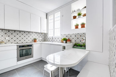This is an example of a mid-sized contemporary l-shaped eat-in kitchen in Montpellier with a drop-in sink, flat-panel cabinets, white cabinets, multi-coloured splashback, cement tile splashback, stainless steel appliances, grey floor, laminate benchtops, ceramic floors, with island and white benchtop.