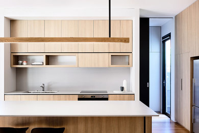 This is an example of a large contemporary galley eat-in kitchen in Melbourne with a double-bowl sink, flat-panel cabinets, medium wood cabinets, quartz benchtops, grey splashback, stainless steel appliances, medium hardwood floors, with island, brown floor and grey benchtop.