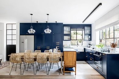 Large elegant l-shaped light wood floor eat-in kitchen photo in Los Angeles with a farmhouse sink, recessed-panel cabinets, blue cabinets, quartz countertops, white backsplash, ceramic backsplash, stainless steel appliances and white countertops