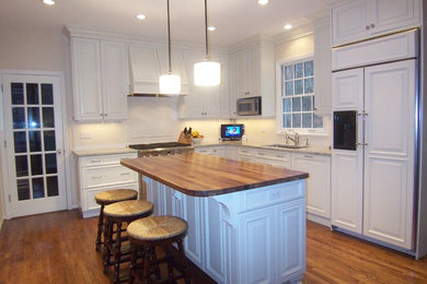 Mid-sized country l-shaped eat-in kitchen in Cincinnati with an undermount sink, raised-panel cabinets, white cabinets, wood benchtops, white splashback, porcelain splashback, panelled appliances, medium hardwood floors and with island.