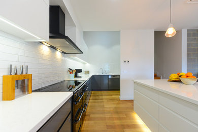 Mid-sized contemporary galley kitchen pantry in Other with a double-bowl sink, grey cabinets, white splashback, subway tile splashback, black appliances, light hardwood floors, with island and brown floor.