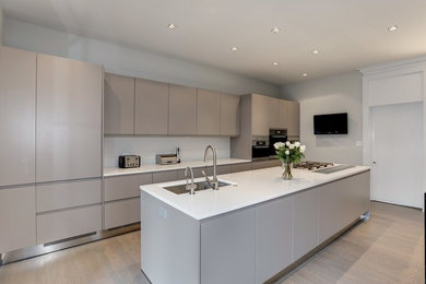 Photo of an expansive modern single-wall eat-in kitchen in DC Metro with an undermount sink, flat-panel cabinets, grey cabinets, quartzite benchtops, stainless steel appliances, light hardwood floors and with island.