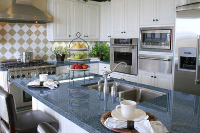 Mid-sized elegant l-shaped dark wood floor and brown floor kitchen photo in San Diego with an undermount sink, raised-panel cabinets, white cabinets, granite countertops, multicolored backsplash, porcelain backsplash, stainless steel appliances and an island