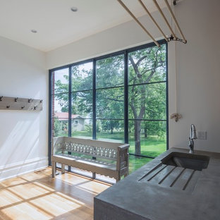 トロントの大きい北欧スタイルのおしゃれな家事室 (コンクリートカウンター、アンダーカウンターシンク、白い壁、淡色無垢フローリング、左右配置の洗濯機・乾燥機、茶色い床) の写真