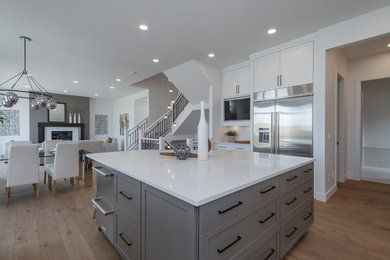 Large minimalist u-shaped medium tone wood floor and brown floor eat-in kitchen photo in Calgary with an undermount sink, shaker cabinets, white cabinets, quartz countertops, white backsplash, window backsplash, stainless steel appliances, an island and white countertops