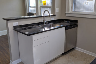Inspiration for a small scandinavian galley porcelain tile and brown floor eat-in kitchen remodel in Other with a single-bowl sink, flat-panel cabinets, white cabinets, granite countertops, black backsplash, stainless steel appliances, no island and black countertops