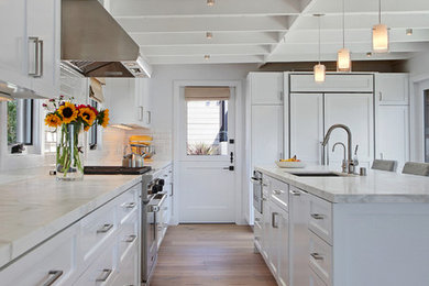Inspiration for a beach style l-shaped kitchen in Orange County with an undermount sink, shaker cabinets, white cabinets, white splashback, panelled appliances, medium hardwood floors and with island.