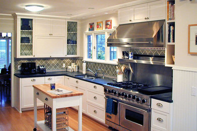 Inspiration for a timeless kitchen remodel in Seattle with glass-front cabinets, stainless steel appliances, wood countertops, a double-bowl sink, white cabinets and green backsplash