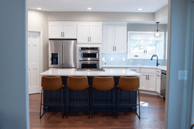 Inspiration for a large transitional medium tone wood floor and brown floor enclosed kitchen remodel in Denver with an undermount sink, shaker cabinets, white cabinets, quartz countertops, blue backsplash, glass tile backsplash, stainless steel appliances, an island and white countertops