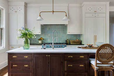 Example of a classic galley medium tone wood floor and brown floor kitchen design in Atlanta with a farmhouse sink, shaker cabinets, white cabinets, blue backsplash, colored appliances, an island and black countertops