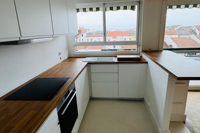 Aménagement d'une cuisine ouverte encastrable et blanche et bois moderne en U de taille moyenne avec un évier encastré, un placard à porte plane, des portes de placard blanches, un plan de travail en stratifié, sol en béton ciré, une péninsule, un sol blanc, un plan de travail marron et fenêtre au-dessus de l'évier.