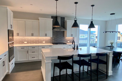 Eat-in kitchen - mid-sized transitional l-shaped dark wood floor and brown floor eat-in kitchen idea in Portland with a farmhouse sink, shaker cabinets, white cabinets, quartz countertops, gray backsplash, porcelain backsplash, stainless steel appliances, an island and white countertops