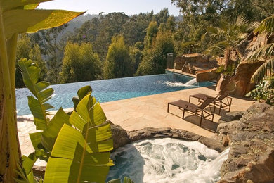 Design ideas for a large tropical backyard rectangular infinity pool in Sacramento with a water slide and stamped concrete.