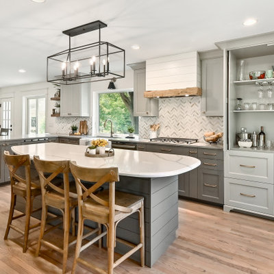 Example of a huge farmhouse l-shaped medium tone wood floor and brown floor eat-in kitchen design in Milwaukee with a farmhouse sink, shaker cabinets, gray cabinets, quartz countertops, white backsplash, marble backsplash, stainless steel appliances, an island and gray countertops